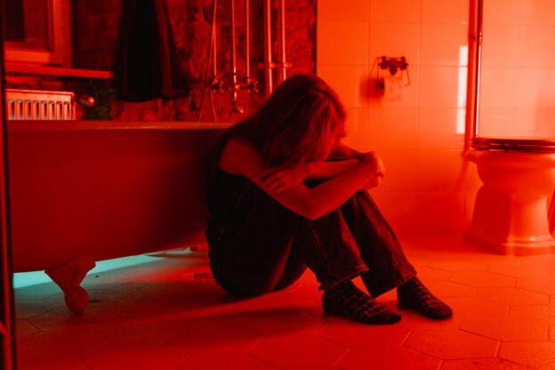Woman sitting on the floor next to a bath tub.