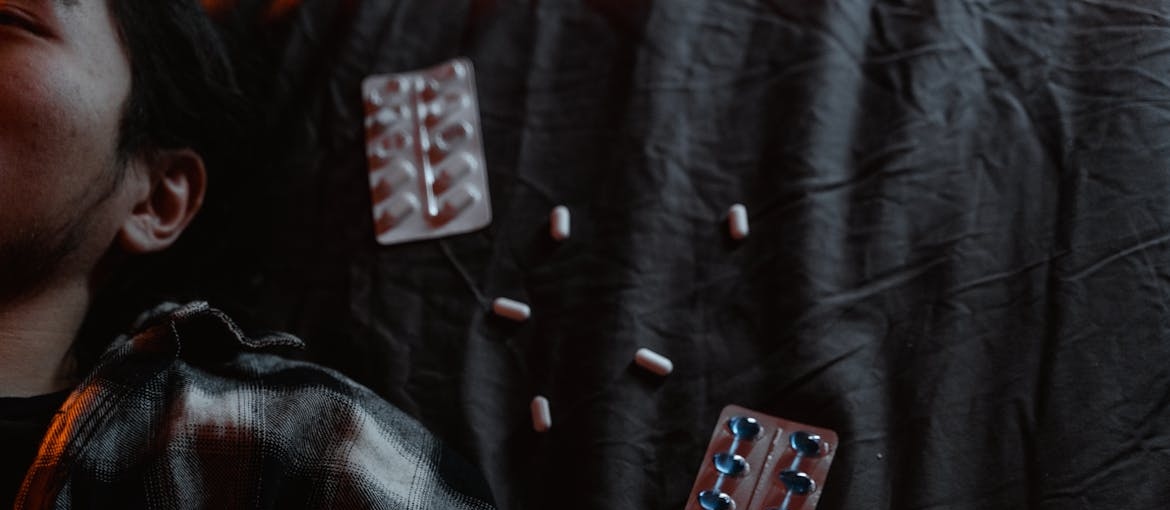 Man lying in bed next to blisters of prescription painkillers.