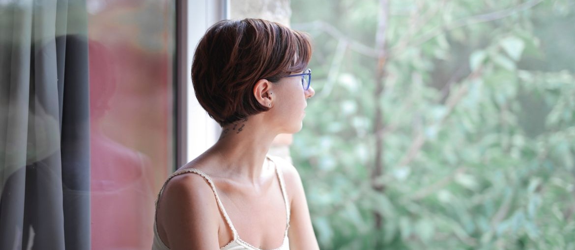 Woman looking out a window while reflecting on thoughts and perception.
