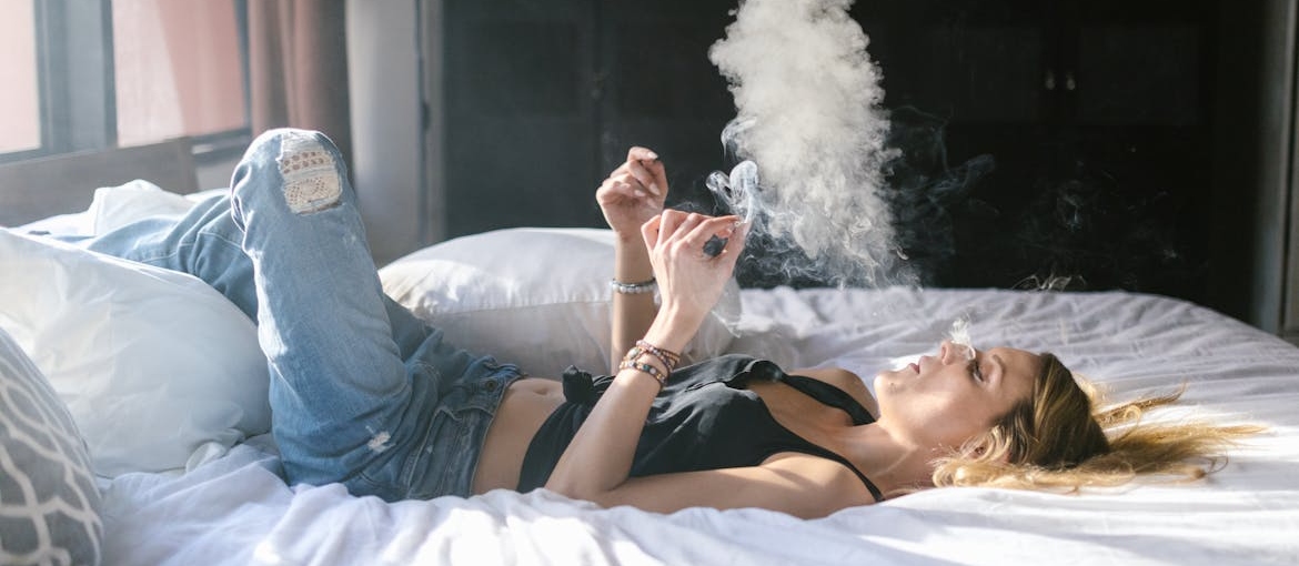Woman lying in bed while smoking marijuana.