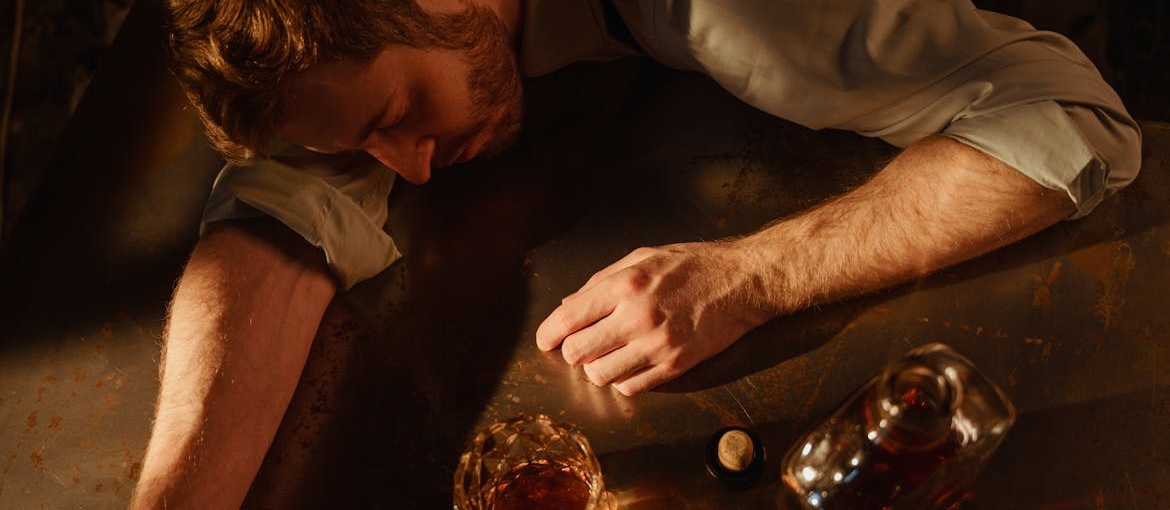 Man sleeping on a table next to a bottle of whiskey.