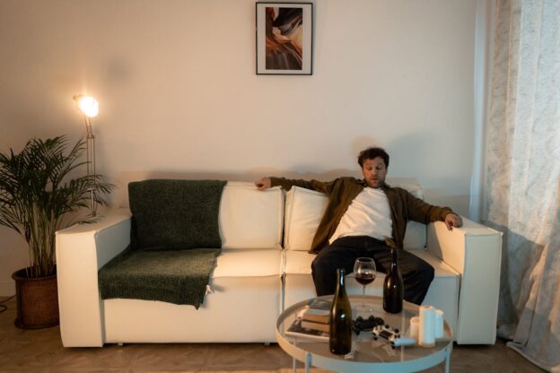 Man sitting on the couch, drinking wine and showing signs of a drinking problem.