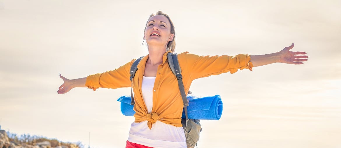 Woman hiking and carrying her yoga mat.