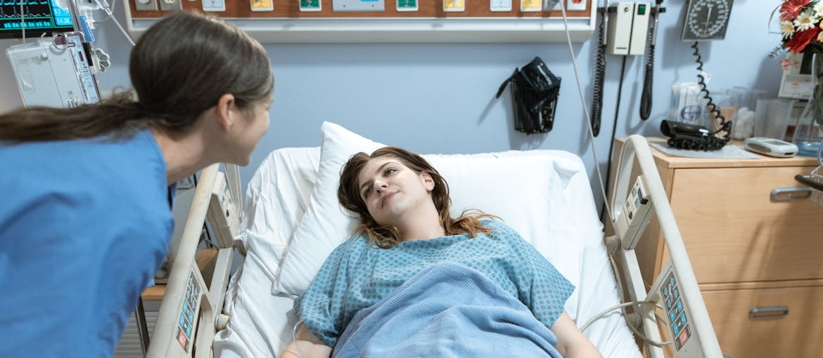 Nurse talking to a woman who is lying in a hospital bed.