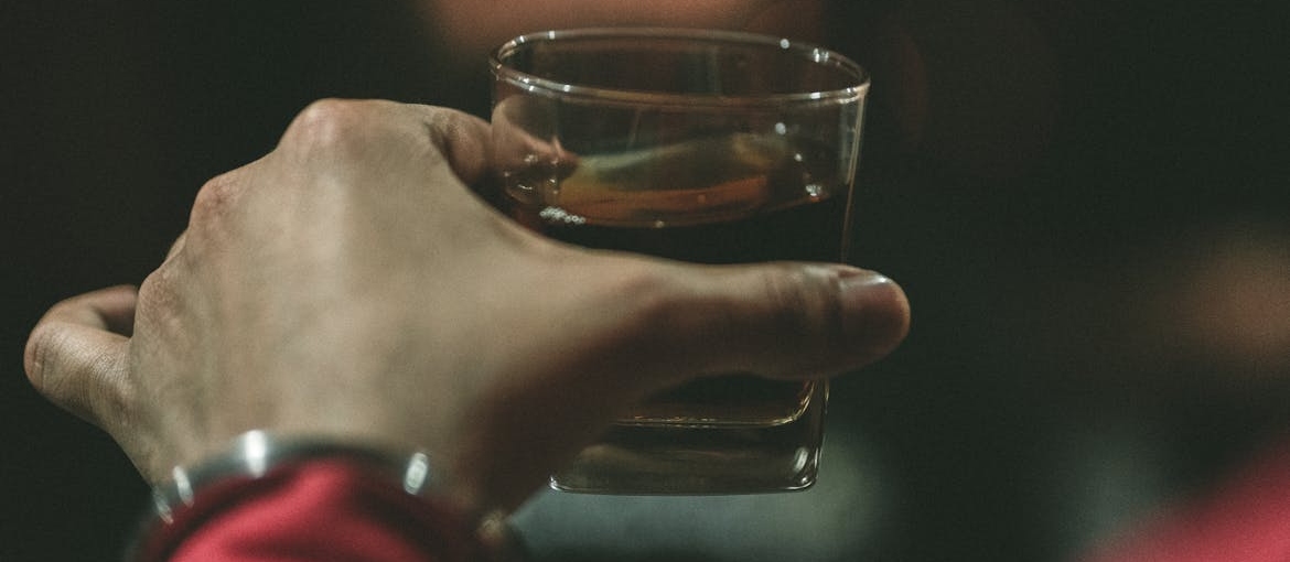 Person holding a glass of whiskey.