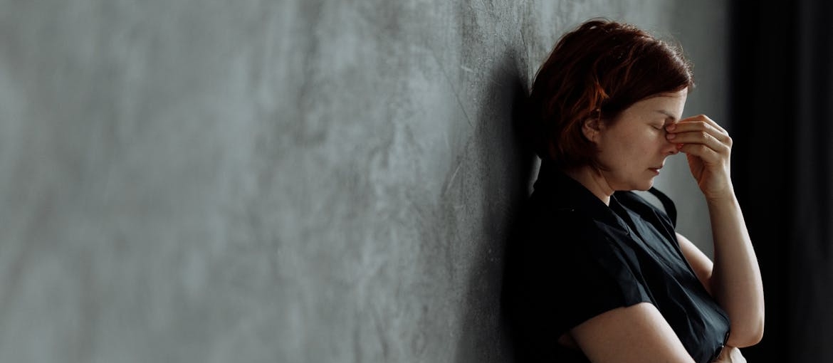 Woman leaning against a wall and pinching the bridge of her nose.
