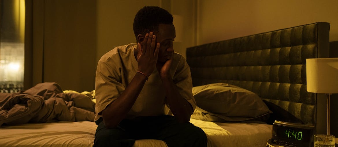 Man experiencing sleep problems in early recovery looking at a clock next to his bed.